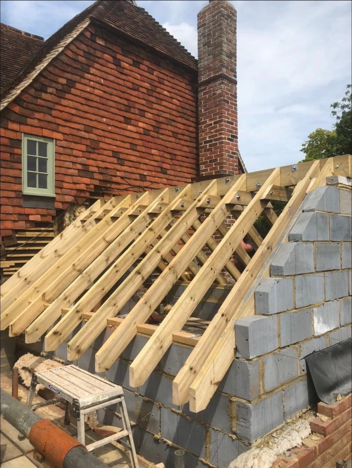 Cut roof rafters framed off a blockwork extension beside a tile-hung elevation
